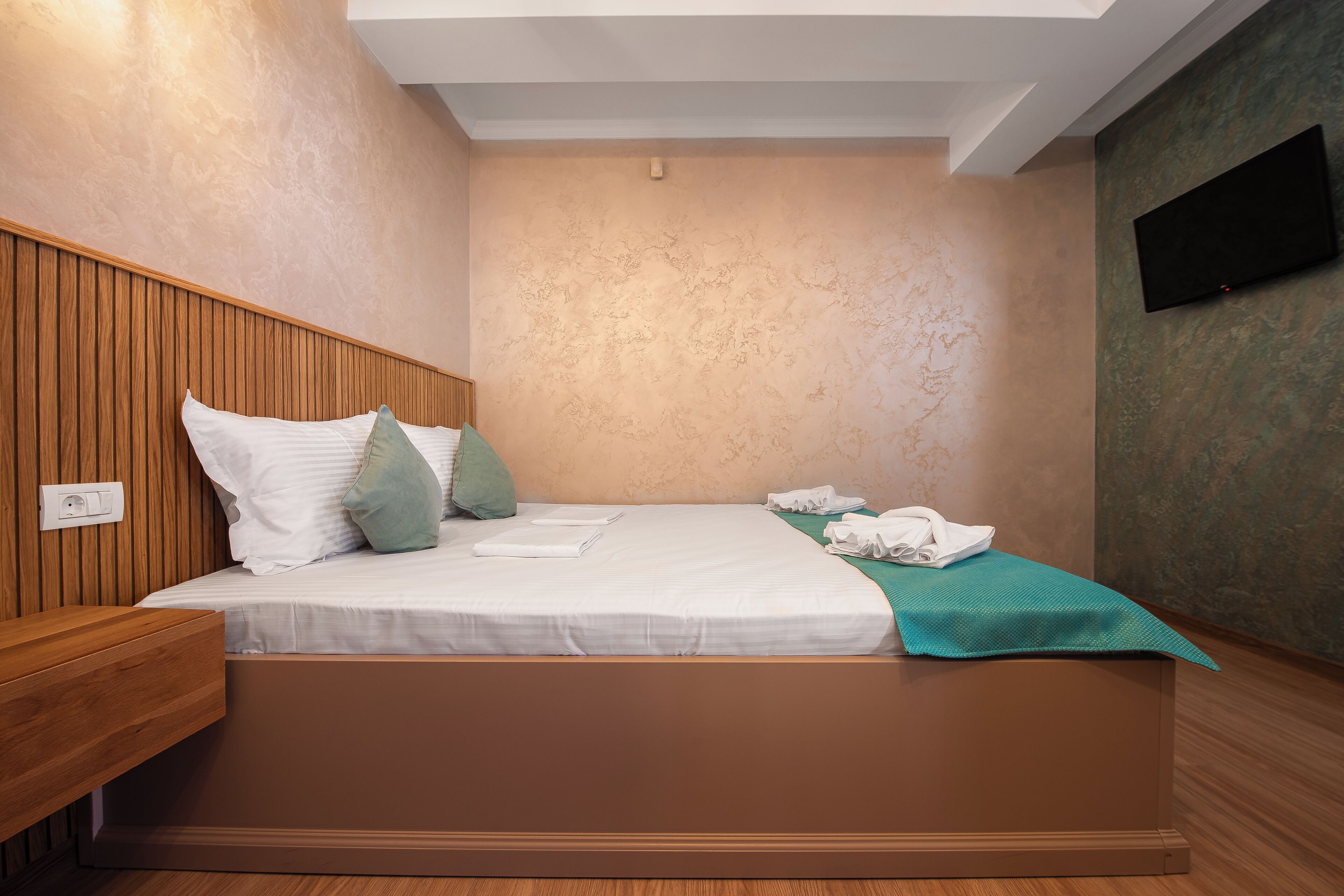 Una habitación de hotel con cama, cabecero de madera, televisor de pantalla plana y una lámpara en el techo.