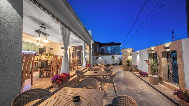 An outdoor patio area with tables and chairs, a kitchen visible through an open door, and potted plants. - Thaya Rooms (Mangalia)