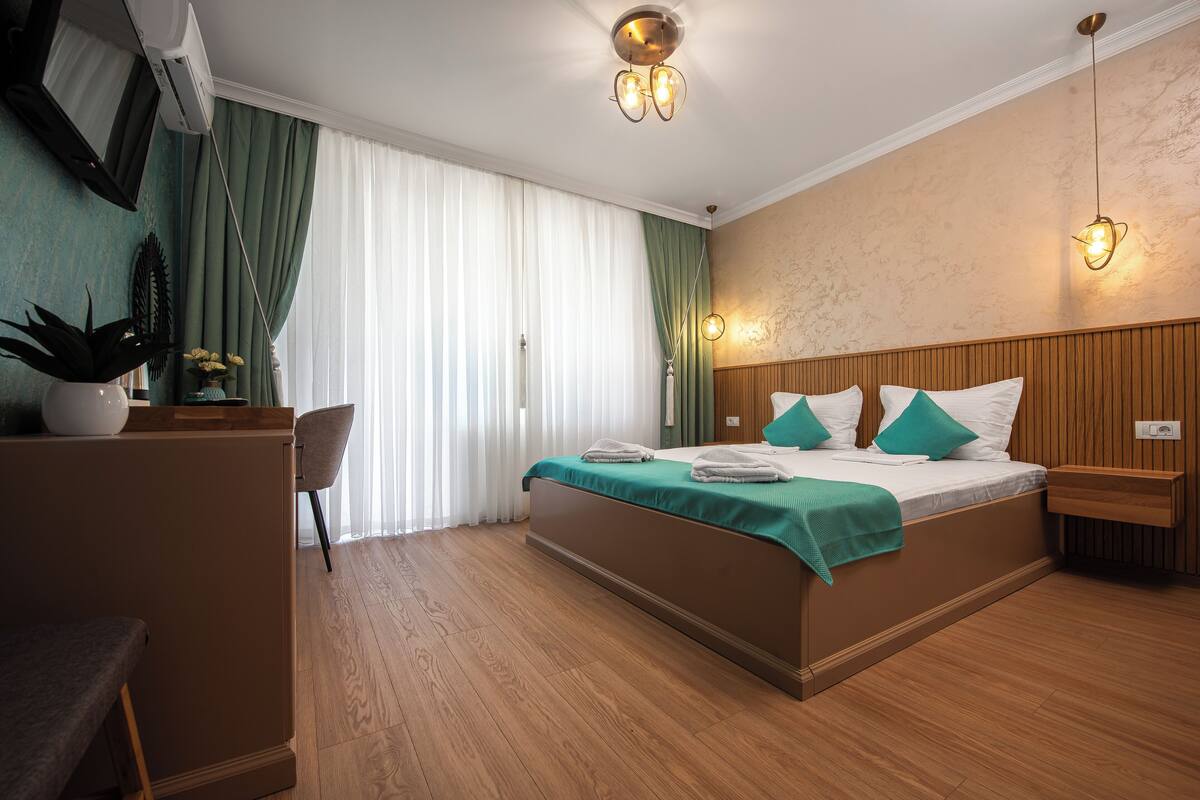 Habitación de hotel con cama, escritorio, silla y un amplio ventanal con cortinas.
