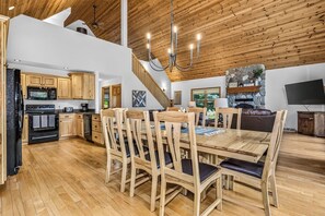 A spacious kitchen with wooden cabinets, a dining area with a large table and chairs, a stone fireplace, and a TV mounted on the wall. - Stepaway Vacation Rentals- Stay-A-While (Eagle River)