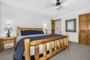 A bedroom with a wooden bed, two bedside tables with lamps, a ceiling fan, and a wooden wardrobe. - Stepaway Vacation Rentals- Stay-A-While (Eagle River)
