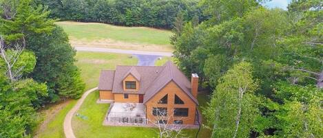 A two-story log cabin with a wrap-around porch, surrounded by dense forest.