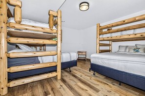 A room with two bunk beds made of wood, a small wooden stool, and a light fixture on the ceiling.