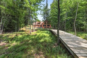 A wooden deck leading to a cabin surrounded by dense forest.