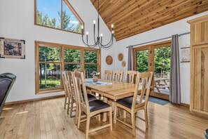Un espace repas avec une table et des chaises en bois, de grandes fenêtres et un lustre.