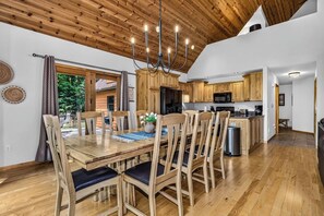 Un vaste espace dédié à la salle à manger, avec une table et des chaises en bois, un lustre et une vue sur l’extérieur.