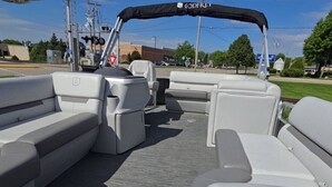 A boat interior with a covered seating area, a control panel, and a view of the surrounding area.