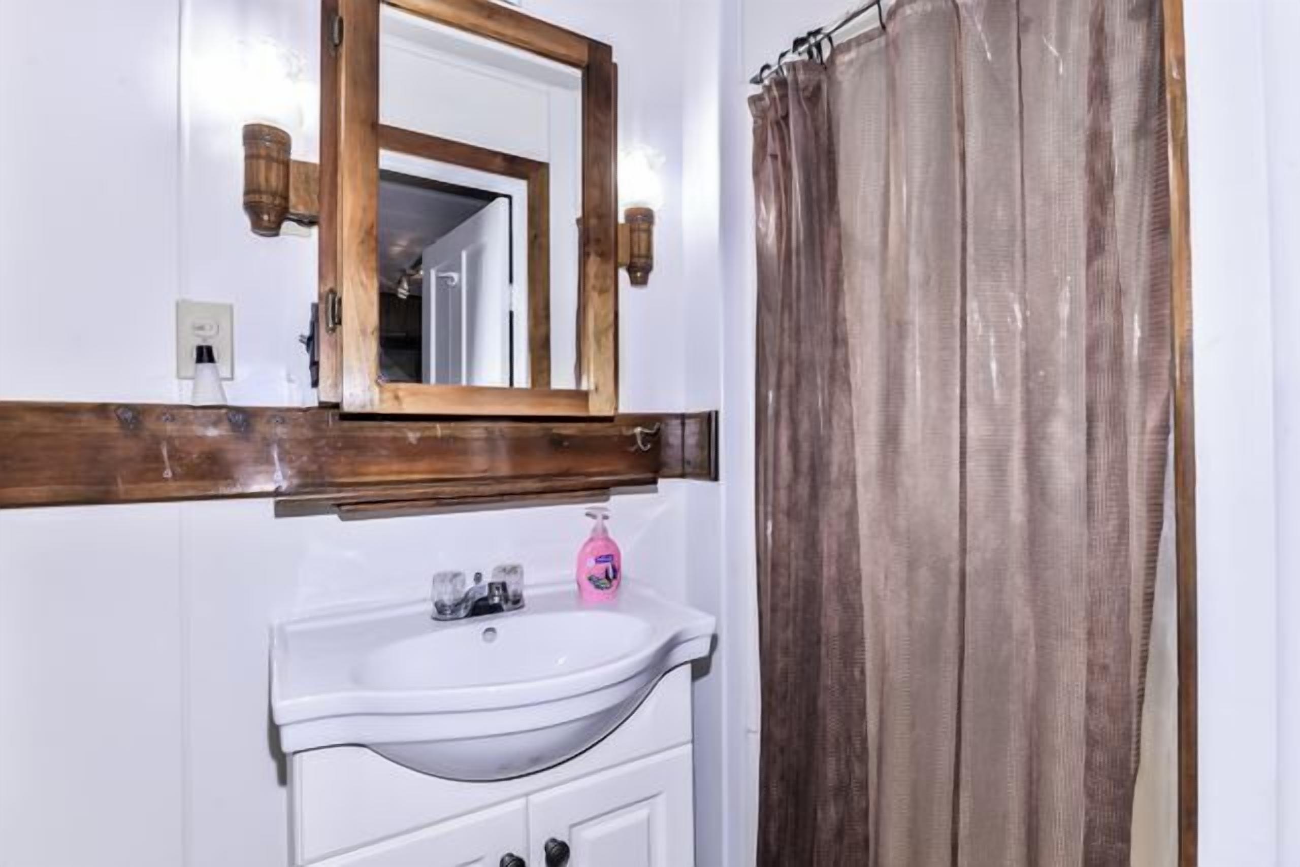 A bathroom with a white sink, a mirror with a wooden frame, and a brown curtain.