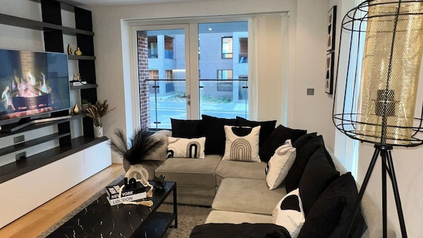 A modern living room with a flat-screen TV, a black coffee table, a beige sofa, and a floor lamp.