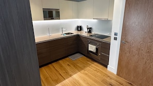 A modern kitchen with wooden flooring, white cabinets, and stainless steel appliances.