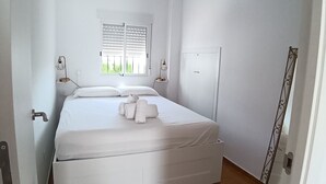 A small, white-walled bedroom with a single bed, a ceiling fan, a window with blinds, and a door with a decorative metal frame. - Charming cottage in a quiet environment (Nerja)