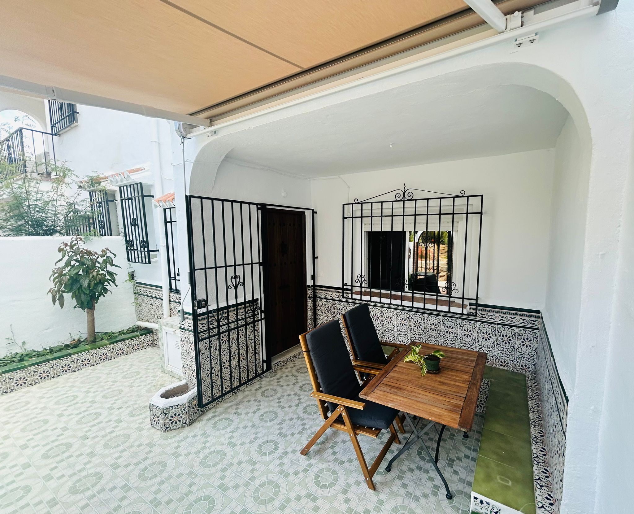 A covered patio area with a wooden table and chairs, a small potted plant, and a decorative metal gate.