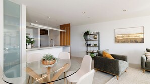 A modern living room with a glass dining table, grey sofa, and a bookshelf.