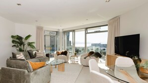 A modern living room with a grey sofa, a glass coffee table, and a TV on the wall.