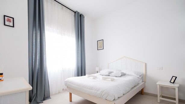 Un dormitorio minimalista con cama, mesita de noche y ventana con cortinas.