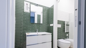 Un baño moderno con paredes de azulejos verdes, un lavamanos blanco y un inodoro.