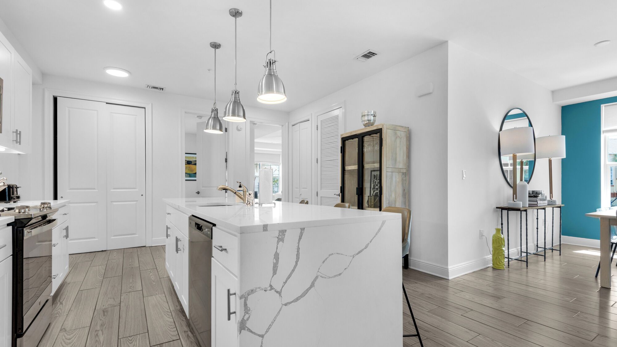 Una cucina moderna con isola in marmo, lampade a sospensione e vista sull'area soggiorno.