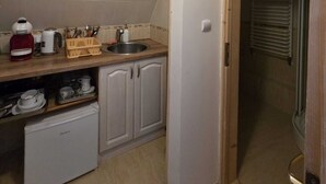 Eine kompakte Küche mit weißen Schränken, einem kleinen Kühlschrank, einer Spüle und einem Wasserkocher auf der Arbeitsplatte.