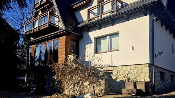 Ein zweistöckiges Haus mit Natursteinfassade, großen Fenstern und einem markanten Giebeldach.