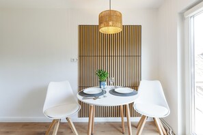 A dining area with a round table, two white chairs, a hanging light fixture, and a vertical wooden panel in the background. - PrimeLoft "Above the rooftops" - Balcony - Old town - Families & groups - View (Goslar)
