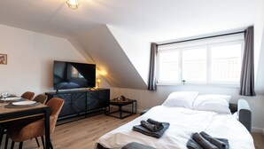 Moderni hotellihuone, jossa on suuri sänky, työpöytä tuoleineen, taulutelevisio ja ikkuna, jossa on verhot.