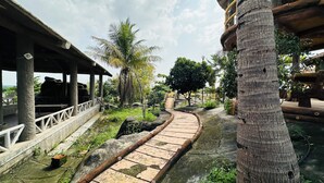 A pathway leading to a covered area with a railing, surrounded by greenery and palm trees. - Rajgadhh Palace Resort (Palanpur)