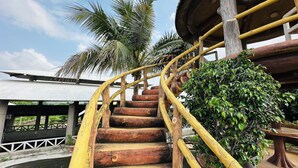 A wooden spiral staircase with a yellow handrail, surrounded by lush greenery and palm trees. - Rajgadhh Palace Resort (Palanpur)