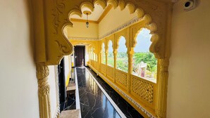 A corridor with ornate yellow and white architectural details, a marble floor, and a view of greenery outside. - Rajgadhh Palace Resort (Palanpur)