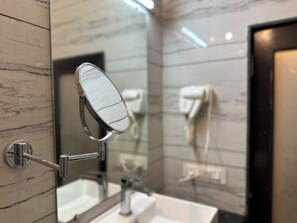 A bathroom with a marble wall, a sink, a mirror, and a hairdryer. - Rajgadhh Palace Resort (Palanpur)