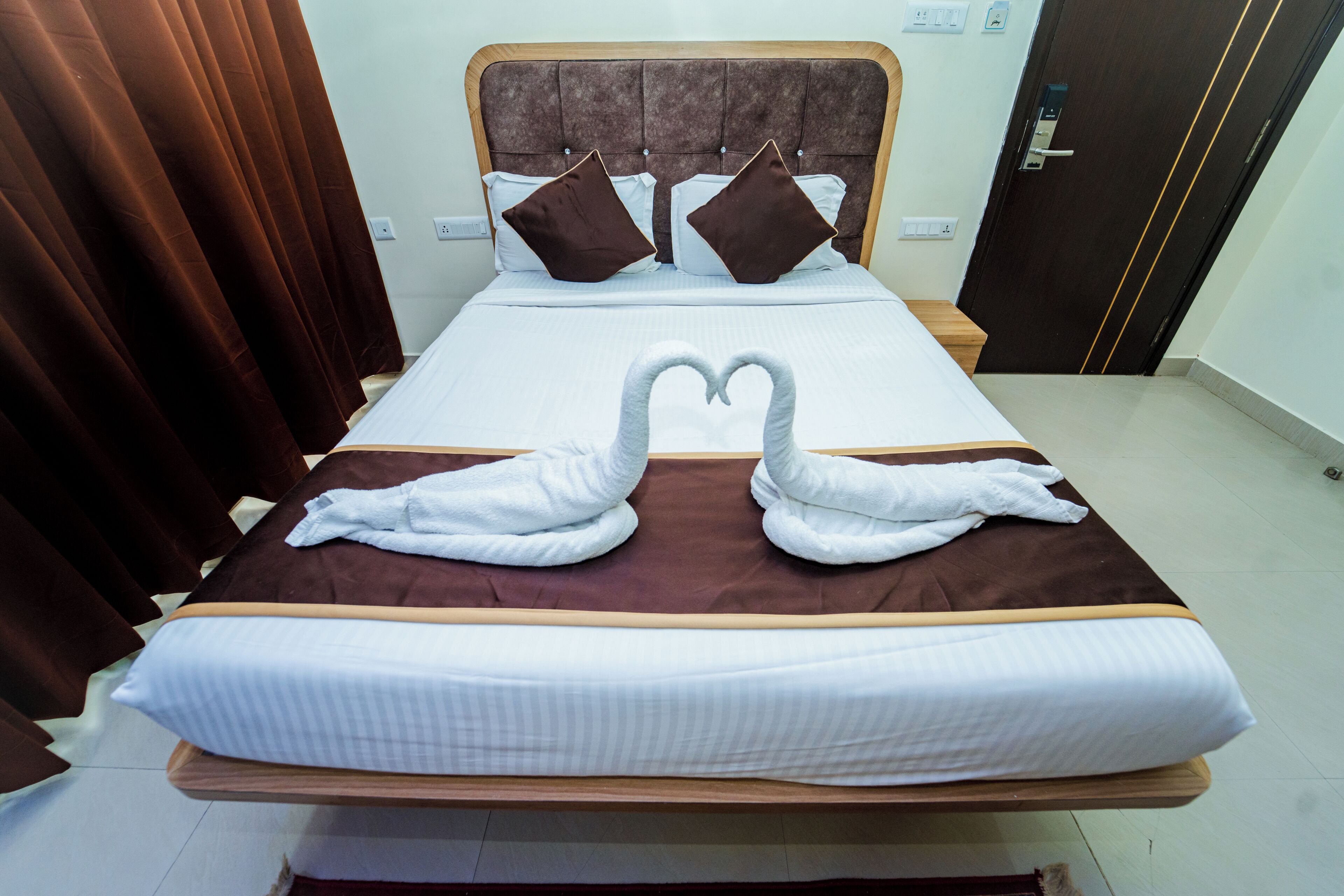 Una cama bien hecha con un cabecero marrón, dos almohadas y dos toallas dispuestas en forma de corazón.