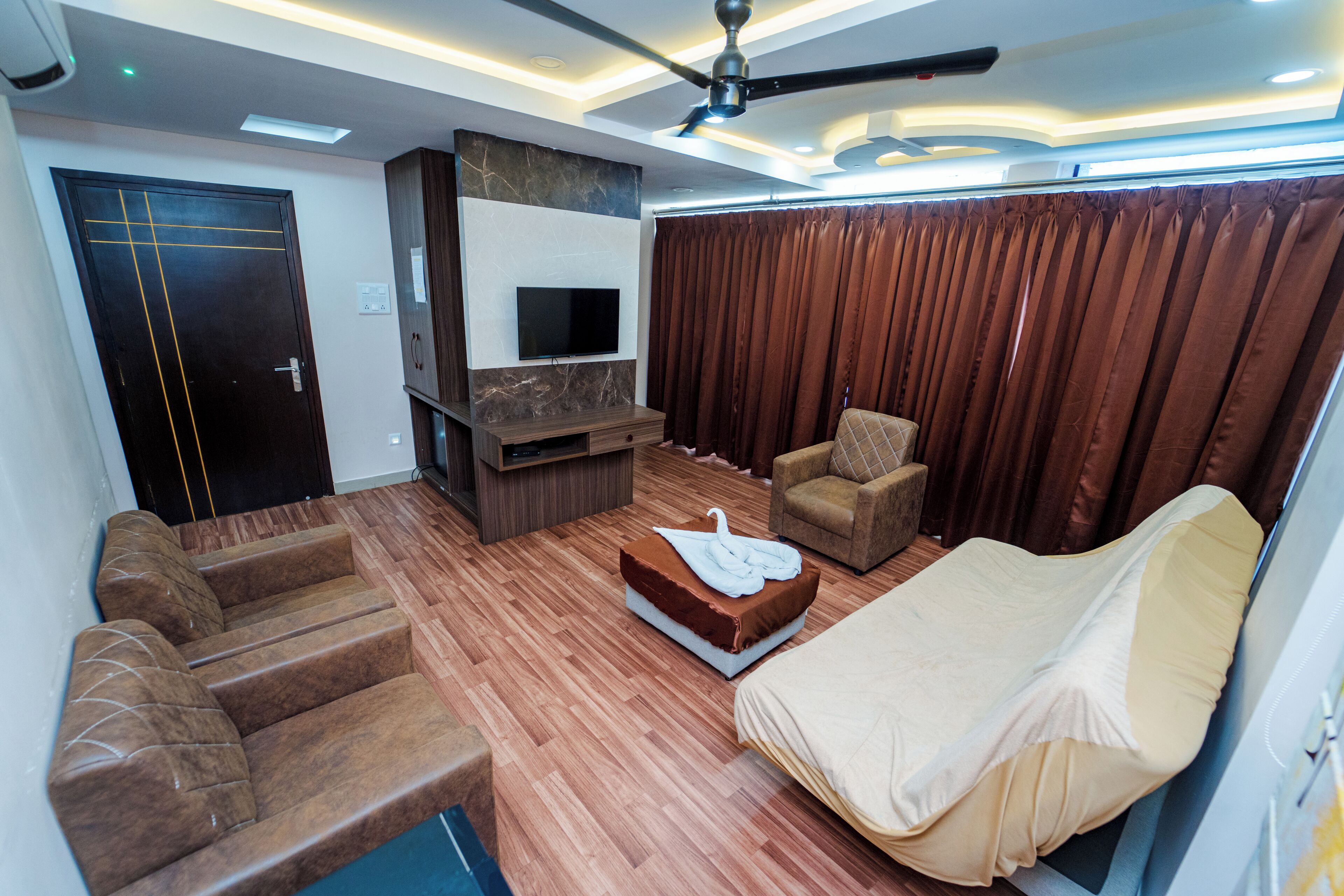 A modern living room with a sofa, a chair, a flat-screen TV, and a ceiling fan.