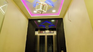 A hallway with a modern ceiling design, a glass elevator, and a marble floor. - Ravila Grand Hotel (Hyderabad)