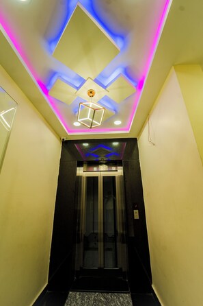 Un couloir doté d’un plafond au design moderne, d’un ascenseur en verre et d’un sol en marbre.