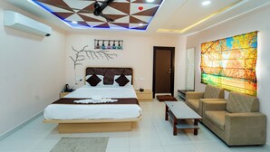 A modern bedroom with a bed, a sofa, a coffee table, a wall art piece, and a ceiling fan. - Ravila Grand Hotel (Hyderabad)