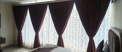 A hotel room with a bed, a ceiling fan, and large windows with curtains.