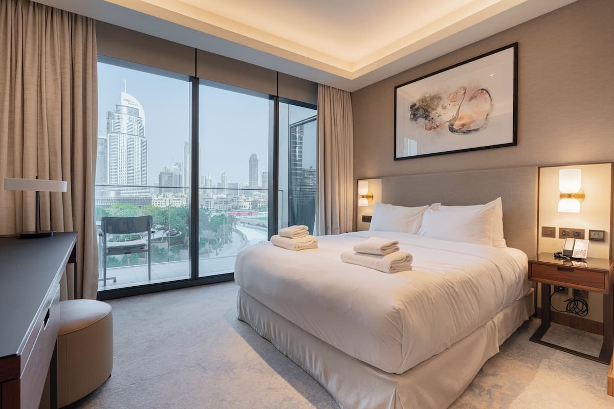 A hotel room with a large bed, a desk, a chair, and a view of the city skyline.