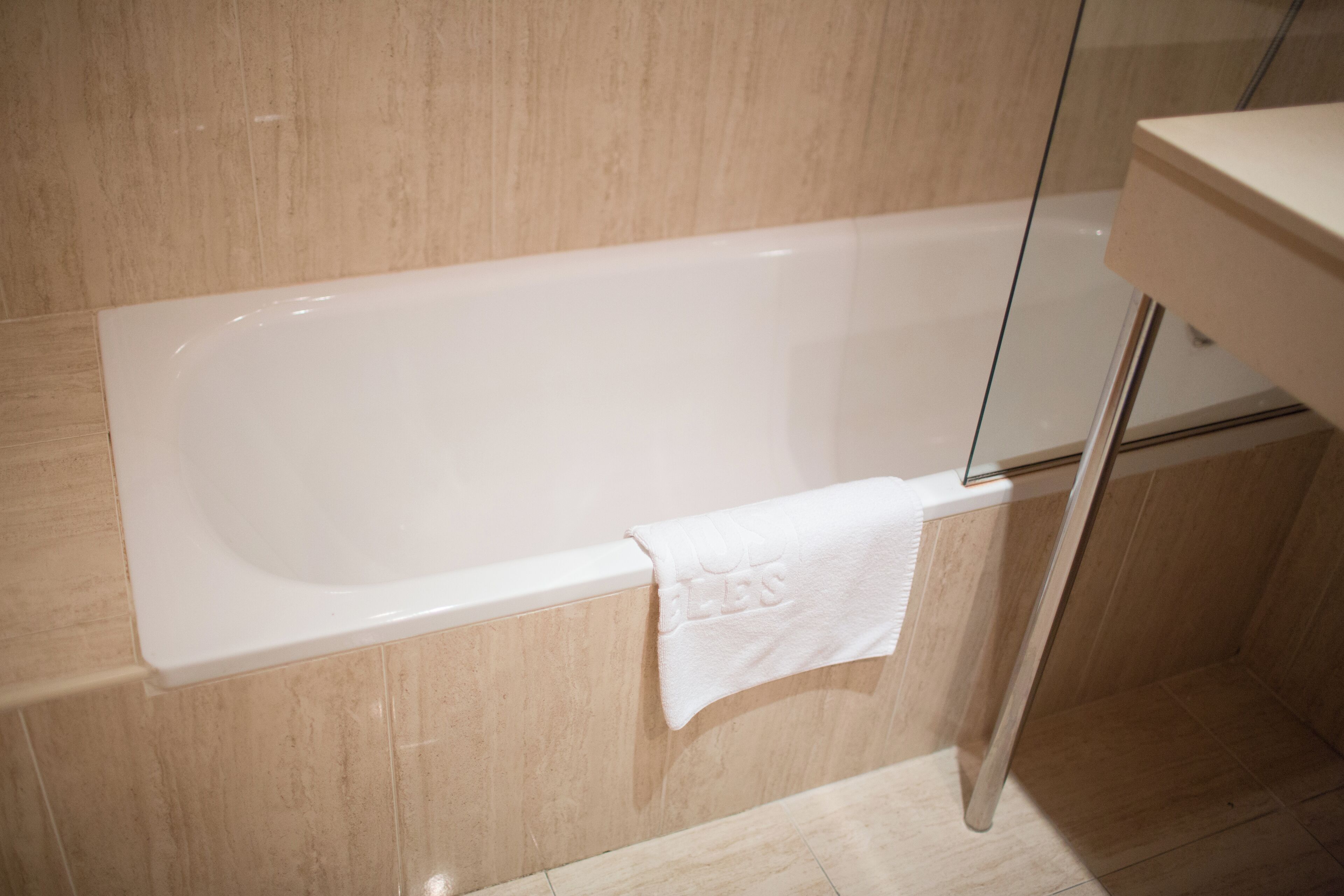 A modern bathroom with a white bathtub, a glass shower enclosure, and a beige tiled wall.