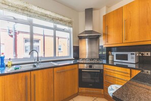A kitchen with wooden cabinets, a stainless steel range hood, a Bosch oven, a microwave, and a window with a view of a brick building.