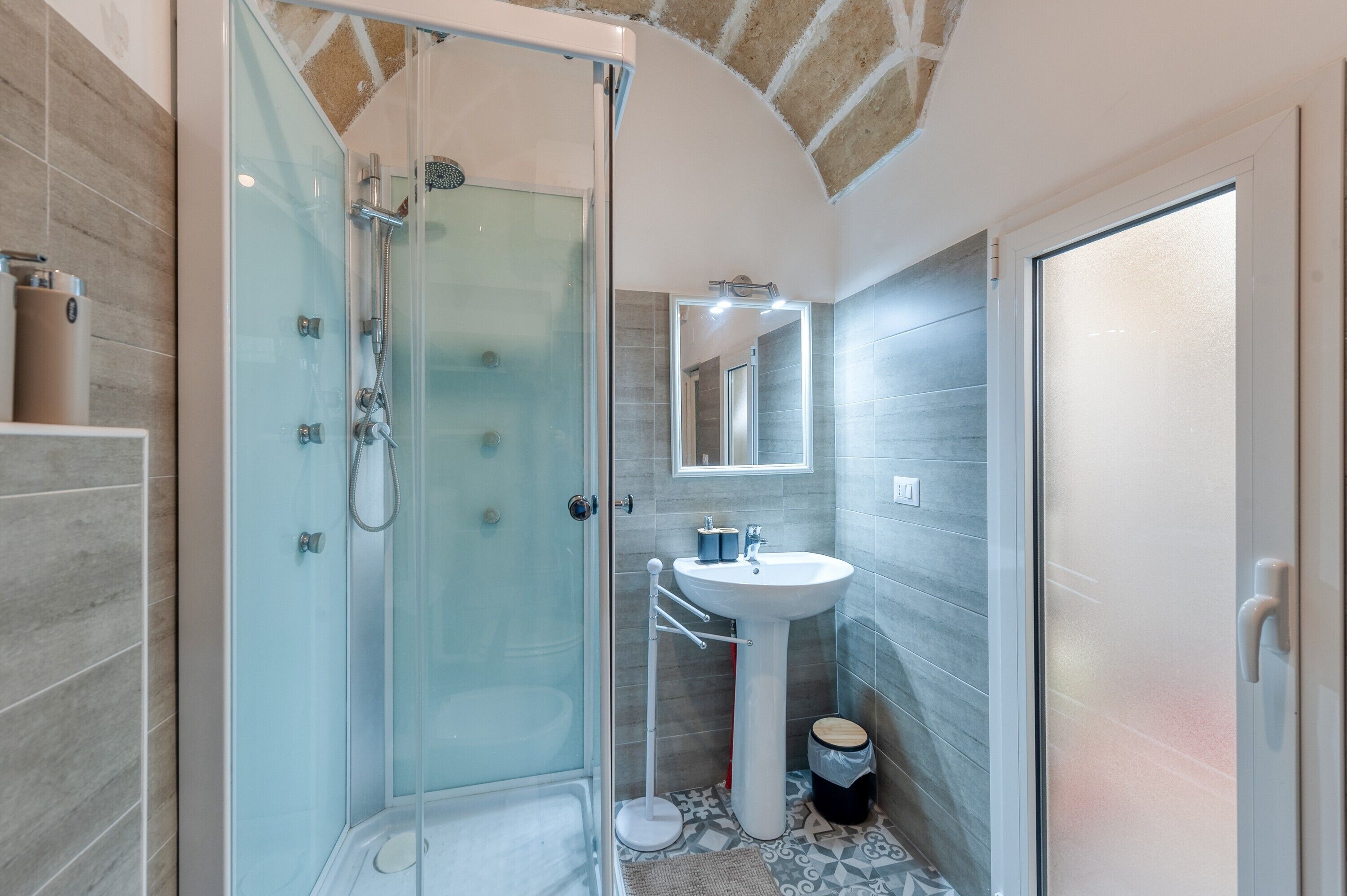 Une salle de bain moderne avec une douche à parois de verre, un lavabo sur colonne et un miroir au-dessus.