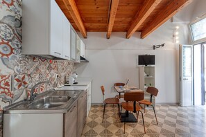 Una cocina con salpicadero de azulejos, vigas de madera en el techo, un lavamanos empotrado y un comedor con sillas y una mesa.