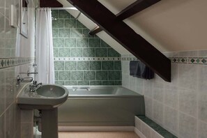 Un baño con lavamanos independiente, bañera y paredes de azulejos verdes.