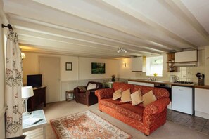 A living room with a red sofa, a television, a small table, and a kitchen area with cabinets and a stove. - Country Dual Cottage Stay | Comfortably Sleeps 6 (Pembrokeshire)