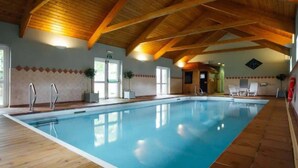 An indoor swimming pool with wooden beams, tiled flooring, and a clear blue pool.