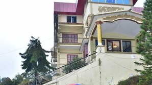 A building with a red roof, a balcony, and a staircase leading up to it. There are two chairs and a colorful umbrella in front of the building. - RAJA STONE PALACE (Kodaikanal)