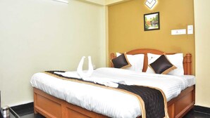 A neatly made bed with a wooden headboard, white bedding, and a black quilted throw. - RAJA STONE PALACE (Kodaikanal)