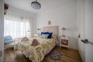 A bedroom with a bed, bedside tables, a window with curtains, a hanging light fixture, and a door.