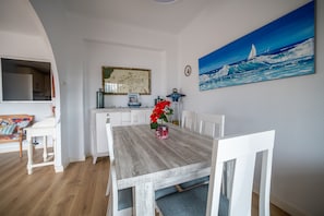 A dining area with a wooden table, white chairs, and a painting of a sailboat on the wall.