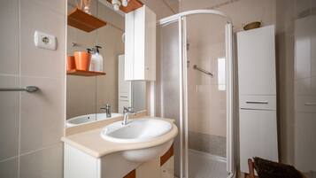 A bathroom with a sink, mirror, shower, and cabinets.