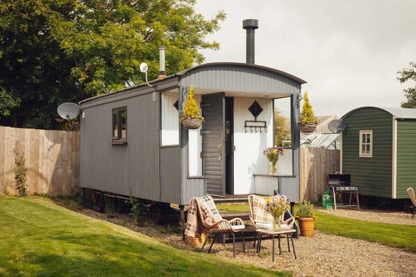 A small, single-story cabin with a chimney, a porch with chairs, and a grill in the backyard.