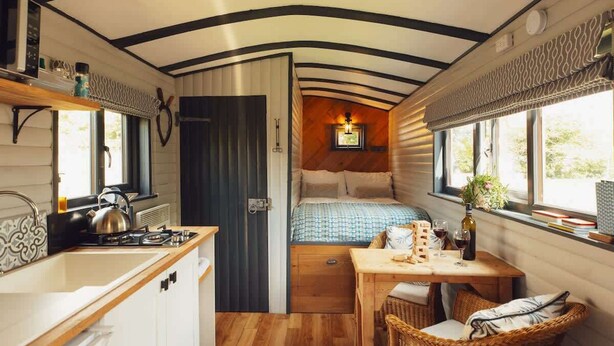 Interior compacto de autocaravana con kitchenette, cama, zona de comedor y pequeña ventana con vistas.